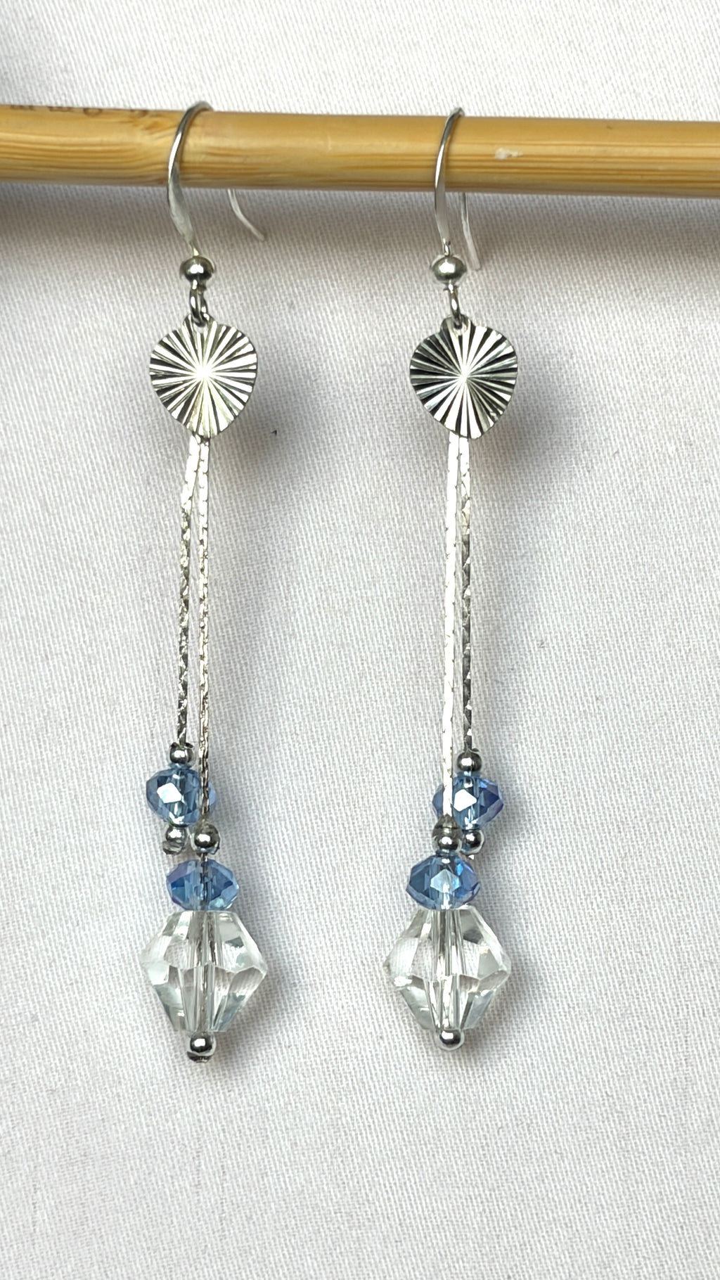 Long silver drop earrings with sunburst disc, hammered bar and pale blue and clear crystal drops hanging from a bamboo rod