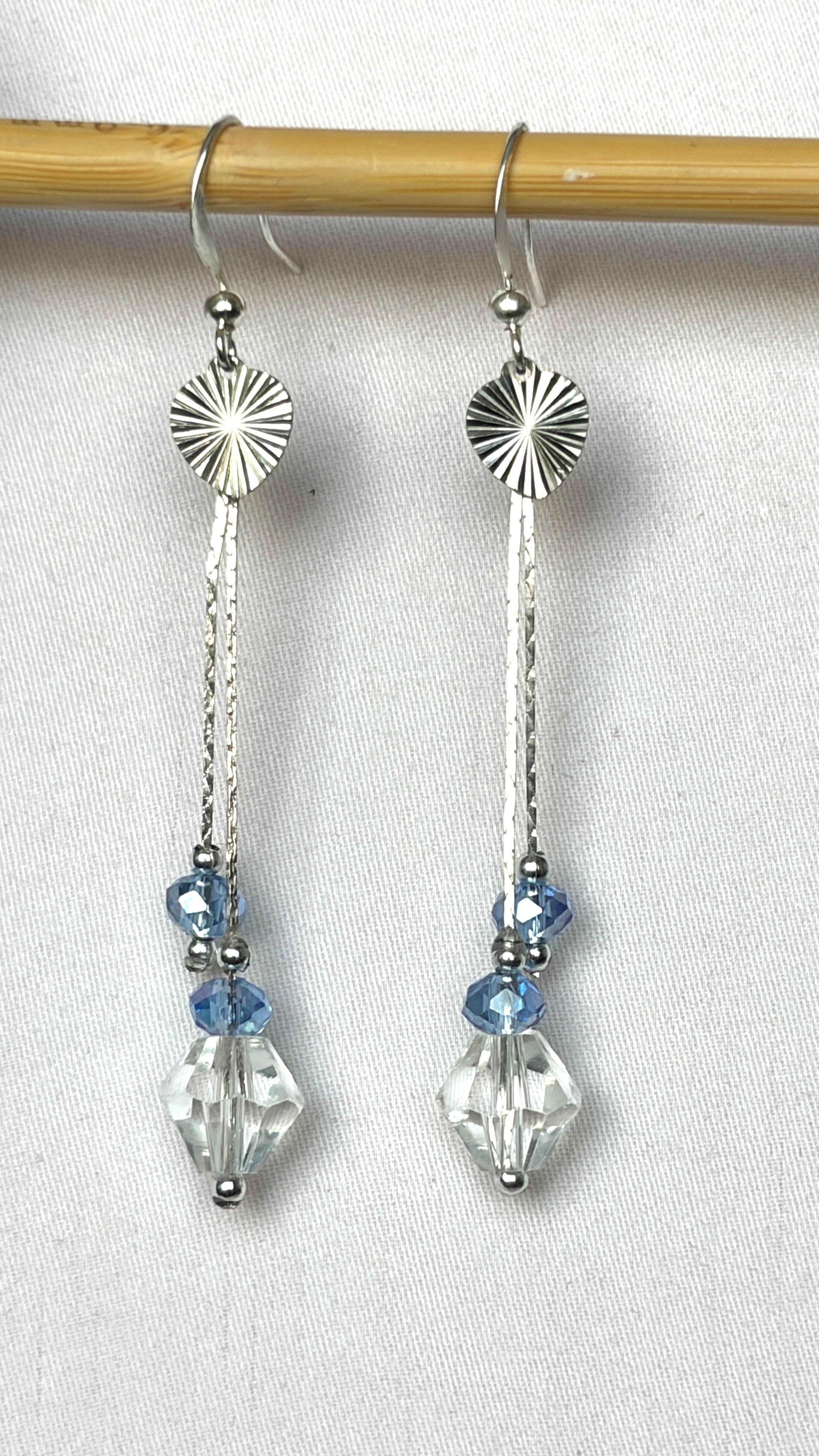 Long silver drop earrings with sunburst disc, hammered bar and pale blue and clear crystal drops hanging from a bamboo rod